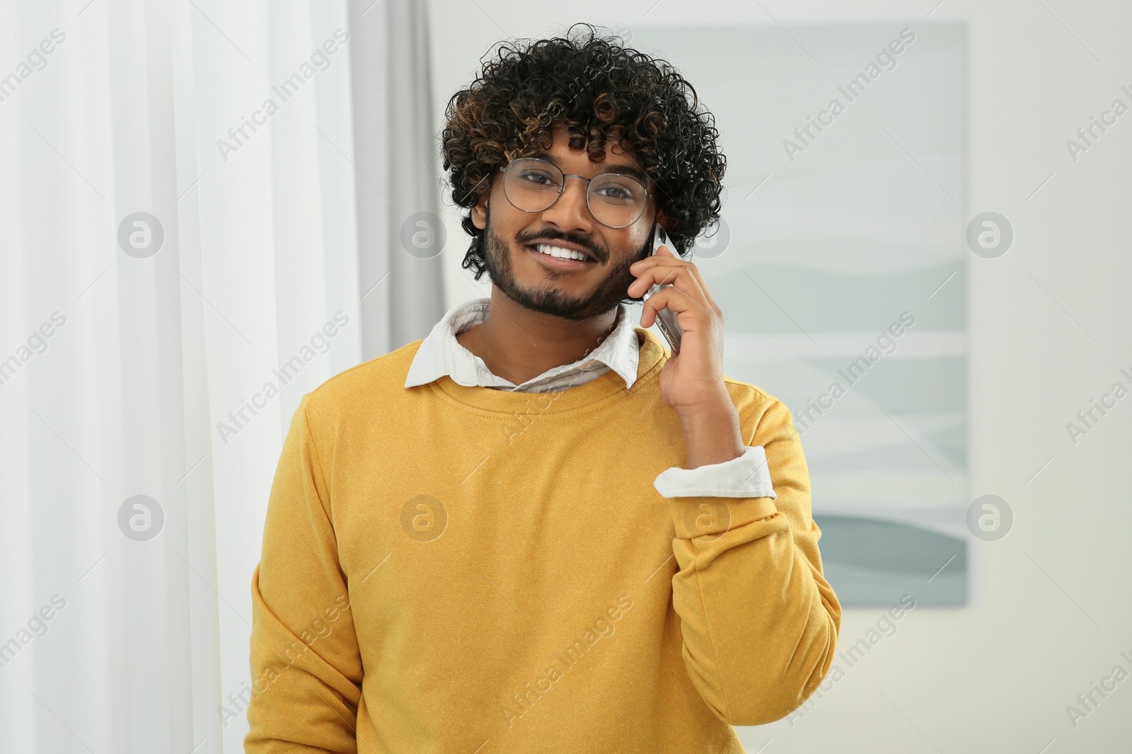 Photo of Handsome smiling man taking over smartphone indoors