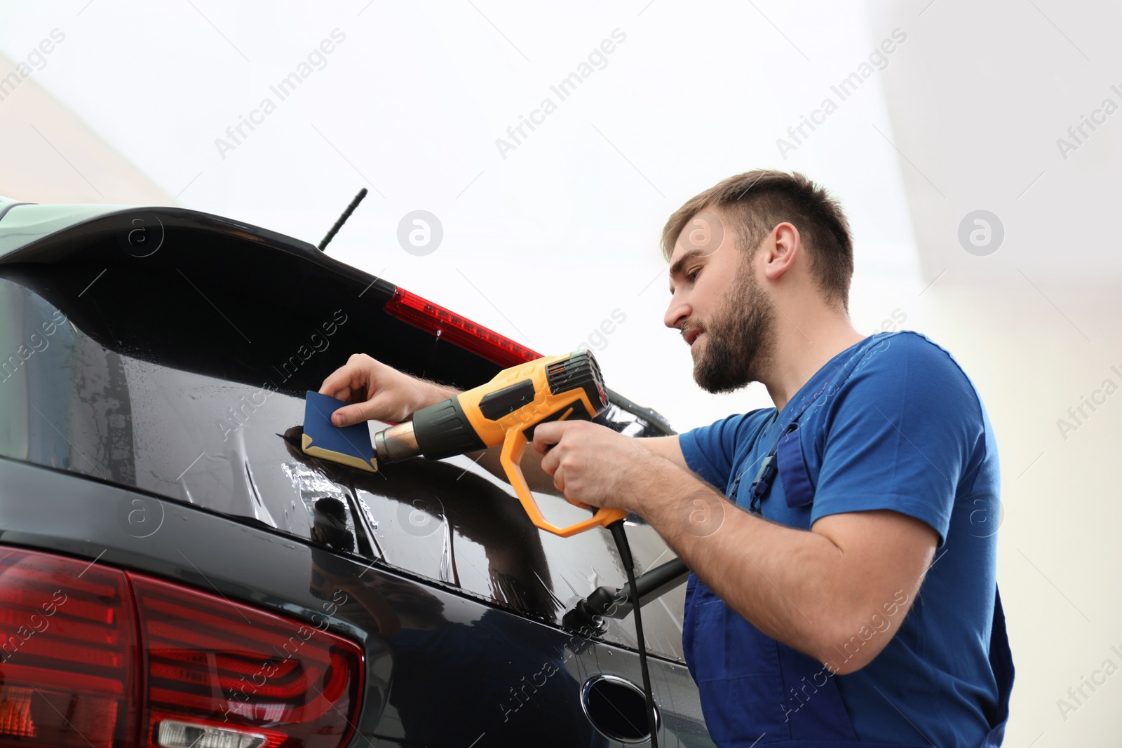 Photo of Worker tinting car window with heat gun in workshop