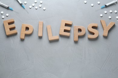 Photo of Word Epilepsy made of wooden letters, pills and syringes on grey table, flat lay. Space for text
