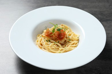 Photo of Tasty spaghetti with prosciutto and microgreens on grey textured table, closeup. Exquisite presentation of pasta dish