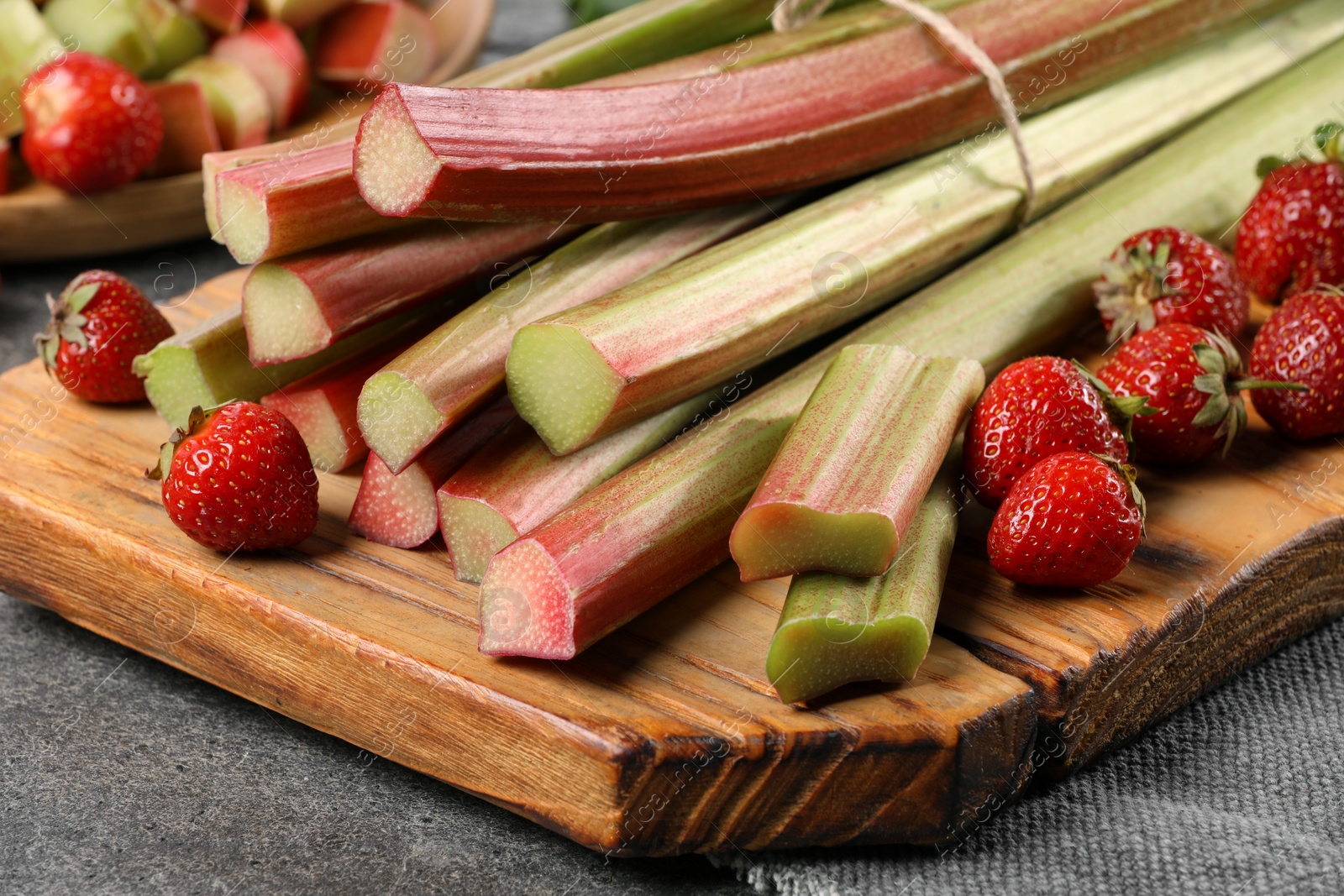 Photo of Fresh ripe rhubarb stalks and strawberries on grey table, closeup