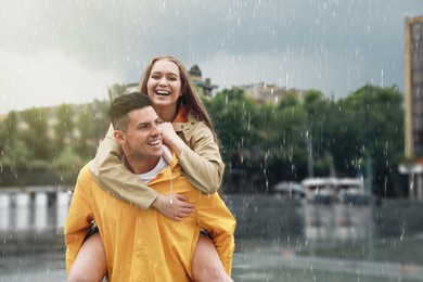 Photo of Lovely couple wearing raincoats under rain on city street