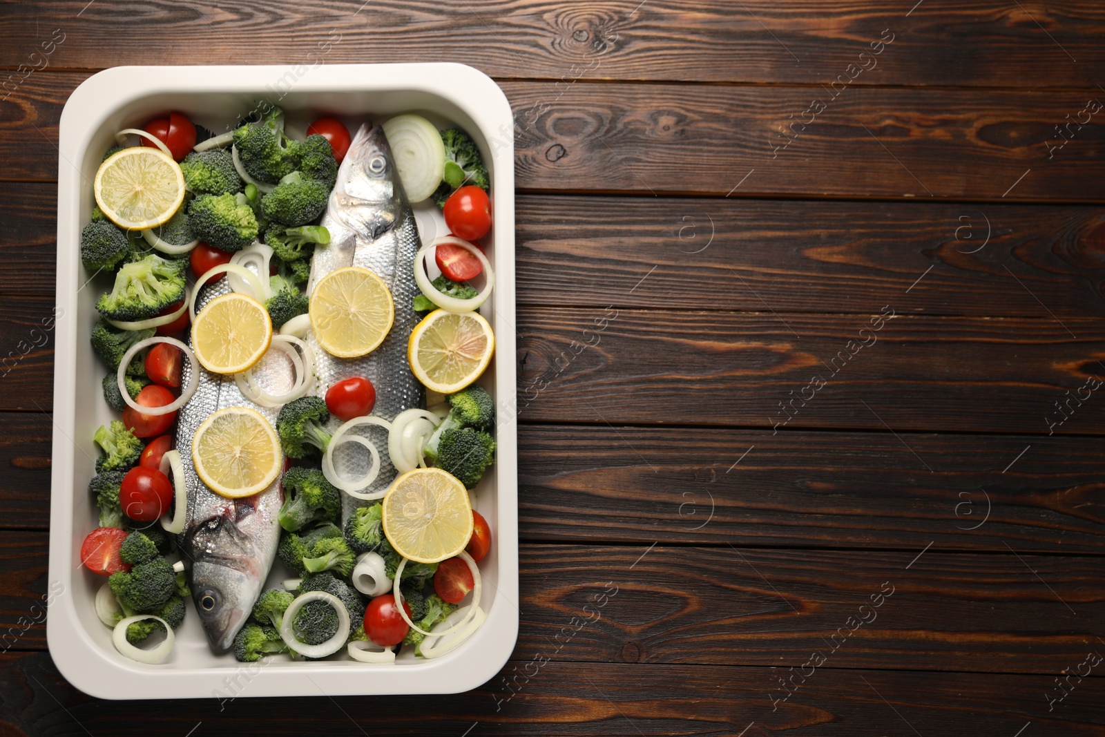 Photo of Raw fish with vegetables and lemon in baking dish on wooden table, top view. Space for text