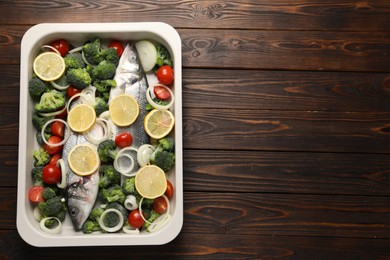 Raw fish with vegetables and lemon in baking dish on wooden table, top view. Space for text