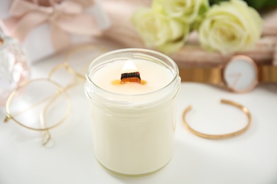 Photo of Burning candle with wooden wick on white table, closeup
