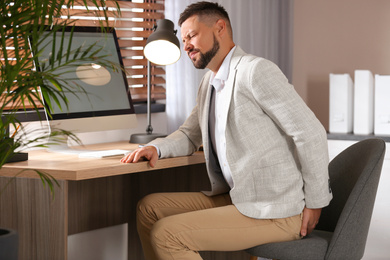 Photo of Man suffering from hemorrhoid at workplace in office