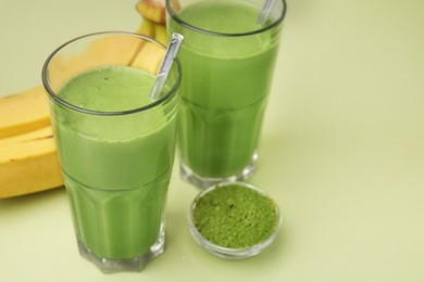 Photo of Glasses of tasty matcha smoothie and powder on pale green background, closeup. Space for text