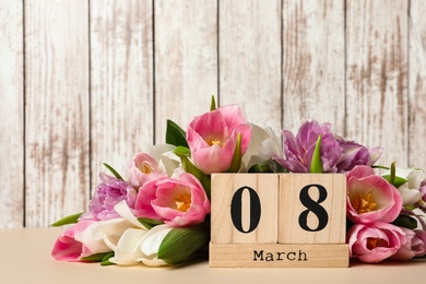 Photo of Block calendar with date 8th of March and tulips on table against wooden background, space for text. International Women's Day