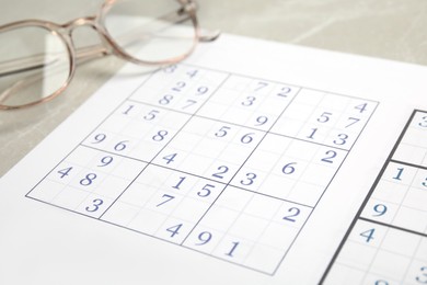 Photo of Sudoku and eyeglasses on table, closeup view