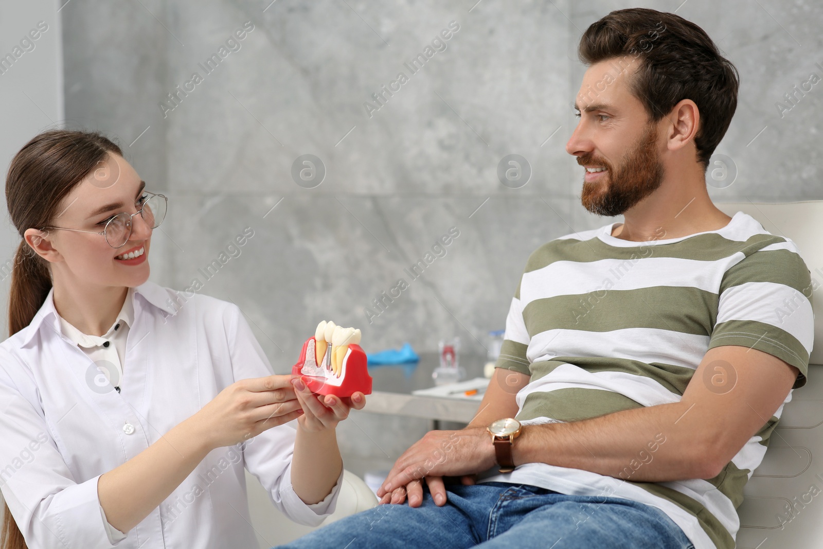 Photo of Doctor with educational model of dental implant consulting patient in clinic