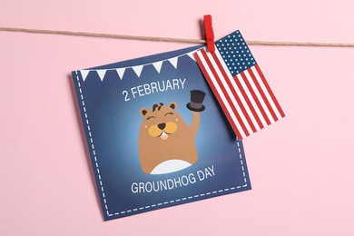Photo of Happy Groundhog Day greeting card and American flag hanging on pink background