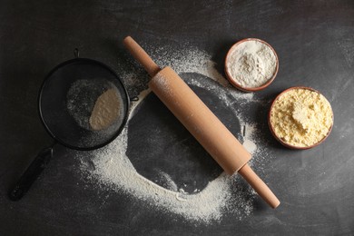 Scattered flour, rolling pin and sieve on black table, flat lay
