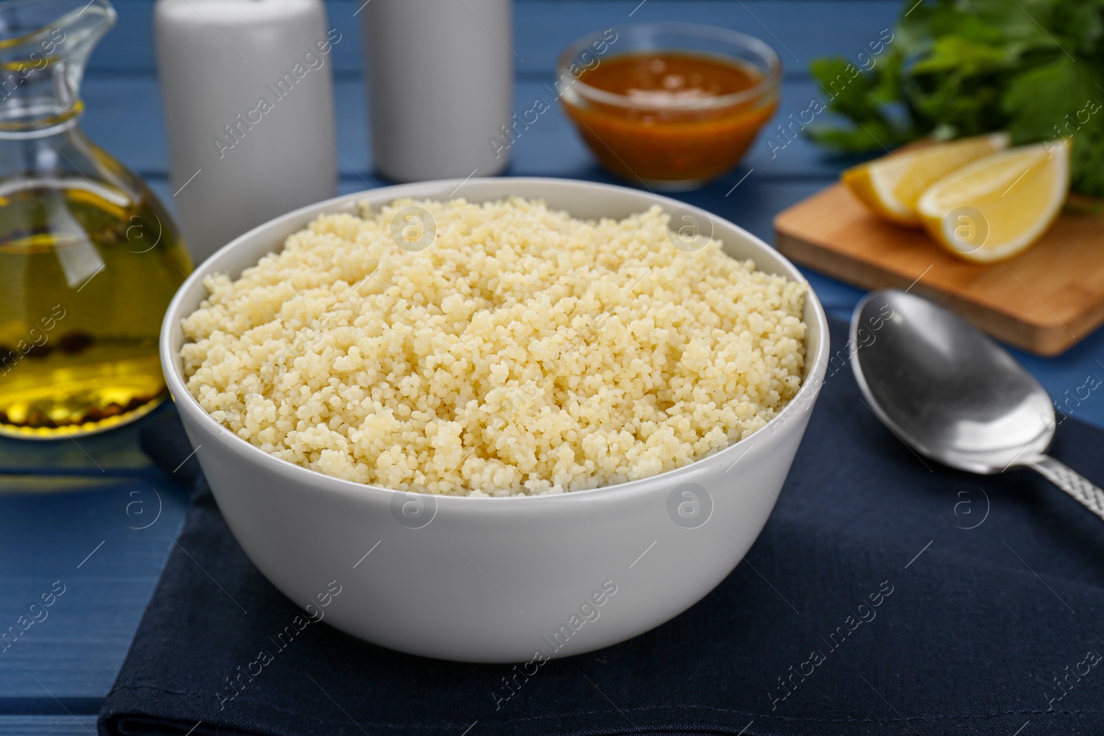 Photo of Bowl of tasty couscous on blue wooden table, closeup