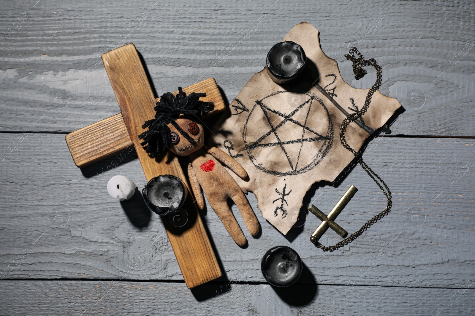 Photo of Female voodoo doll with heart and ceremonial items on grey wooden table, flat lay