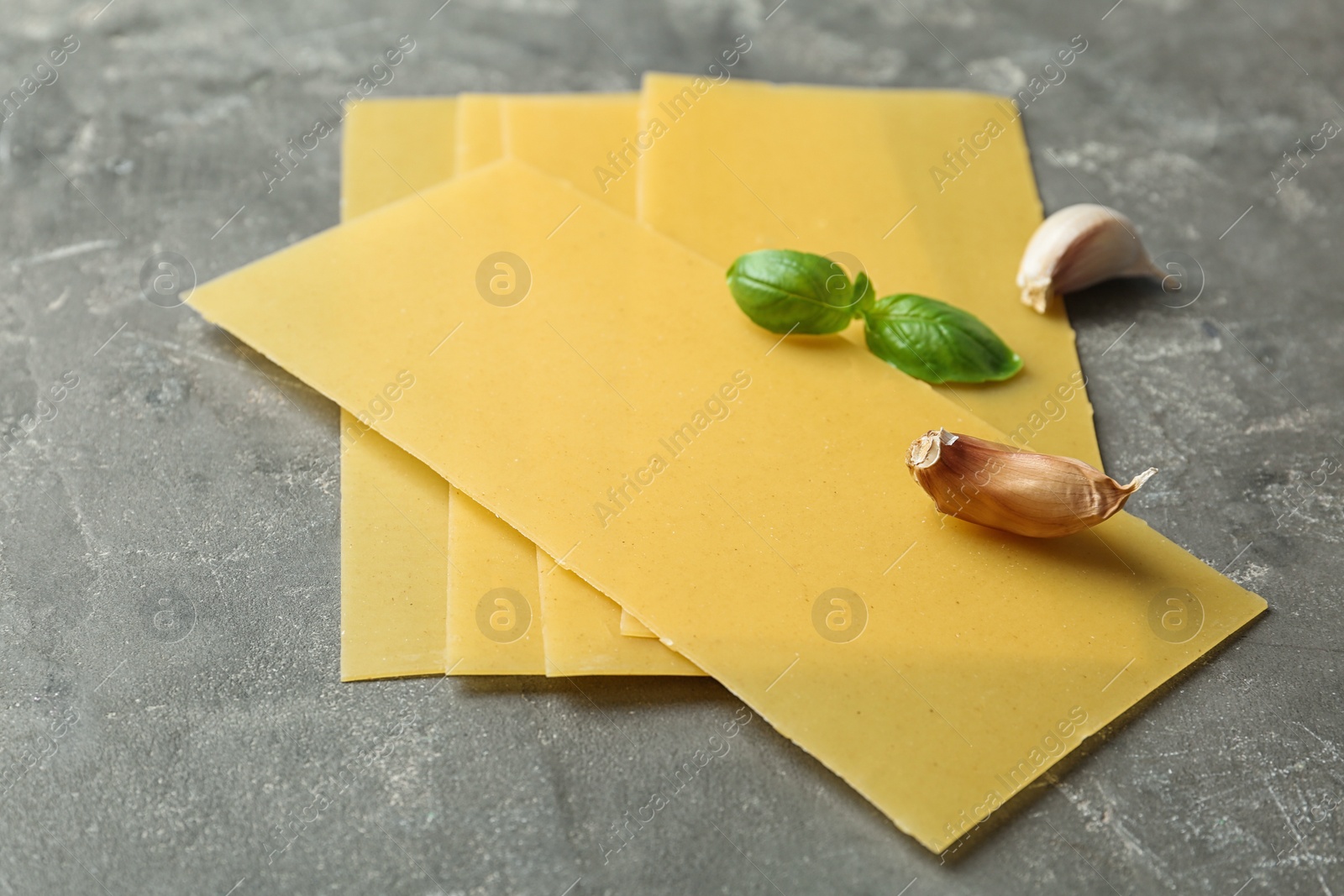 Photo of Uncooked lasagna sheets, garlic and basil on dark table