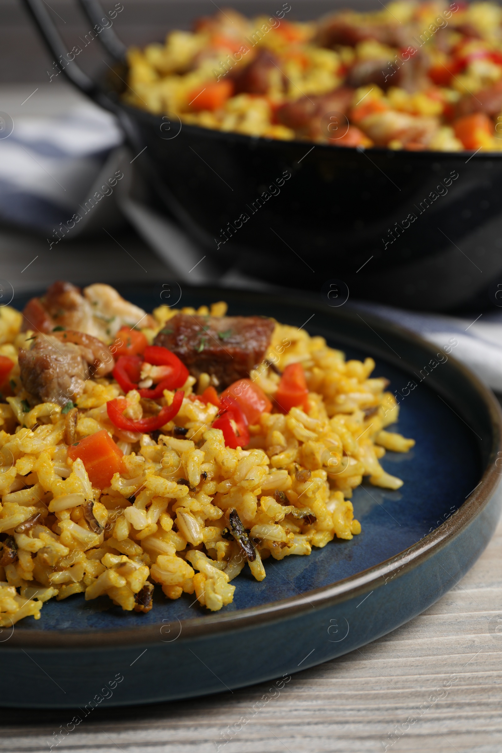 Photo of Delicious pilaf with meat, carrot and chili pepper on wooden table, closeup