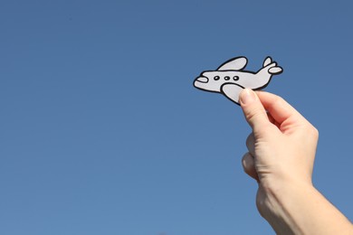 Photo of Woman holding paper plane against blue sky, closeup. Space for text