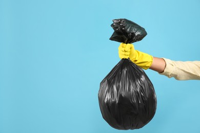Photo of Woman holding full garbage bag on light blue background, closeup. Space for text
