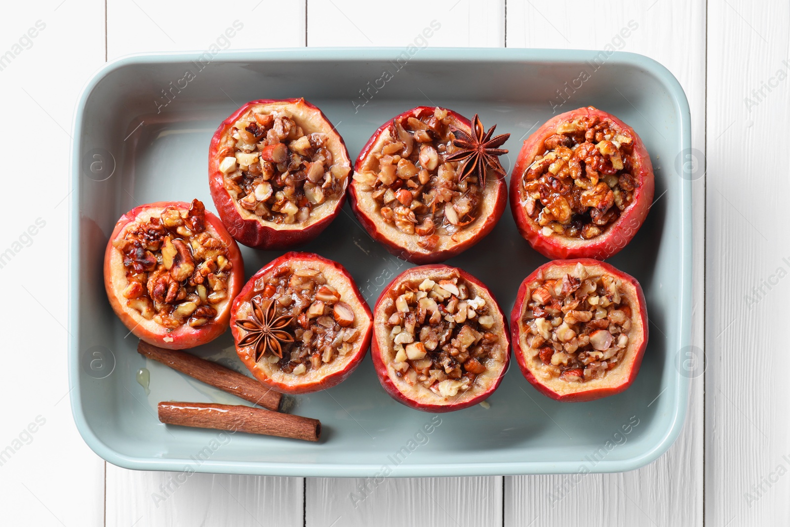 Photo of Tasty baked apples with nuts, honey and spices in dish on white wooden table, top view