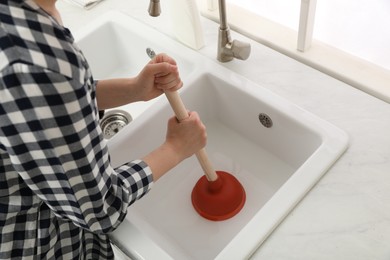 Woman using plunger to unclog sink drain in kitchen, closeup