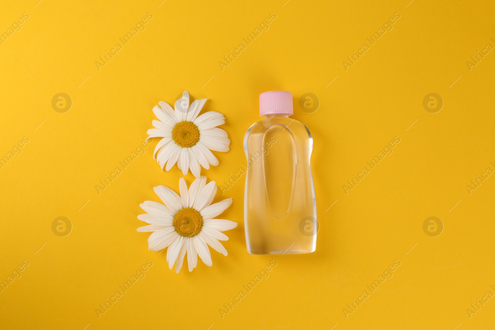 Photo of Bottle with baby oil and daisies on orange background, flat lay
