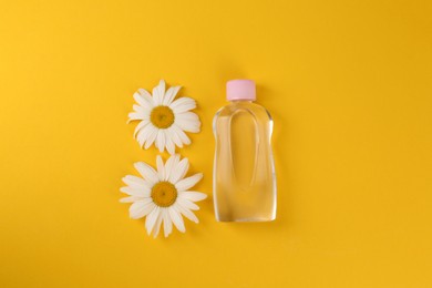 Bottle with baby oil and daisies on orange background, flat lay