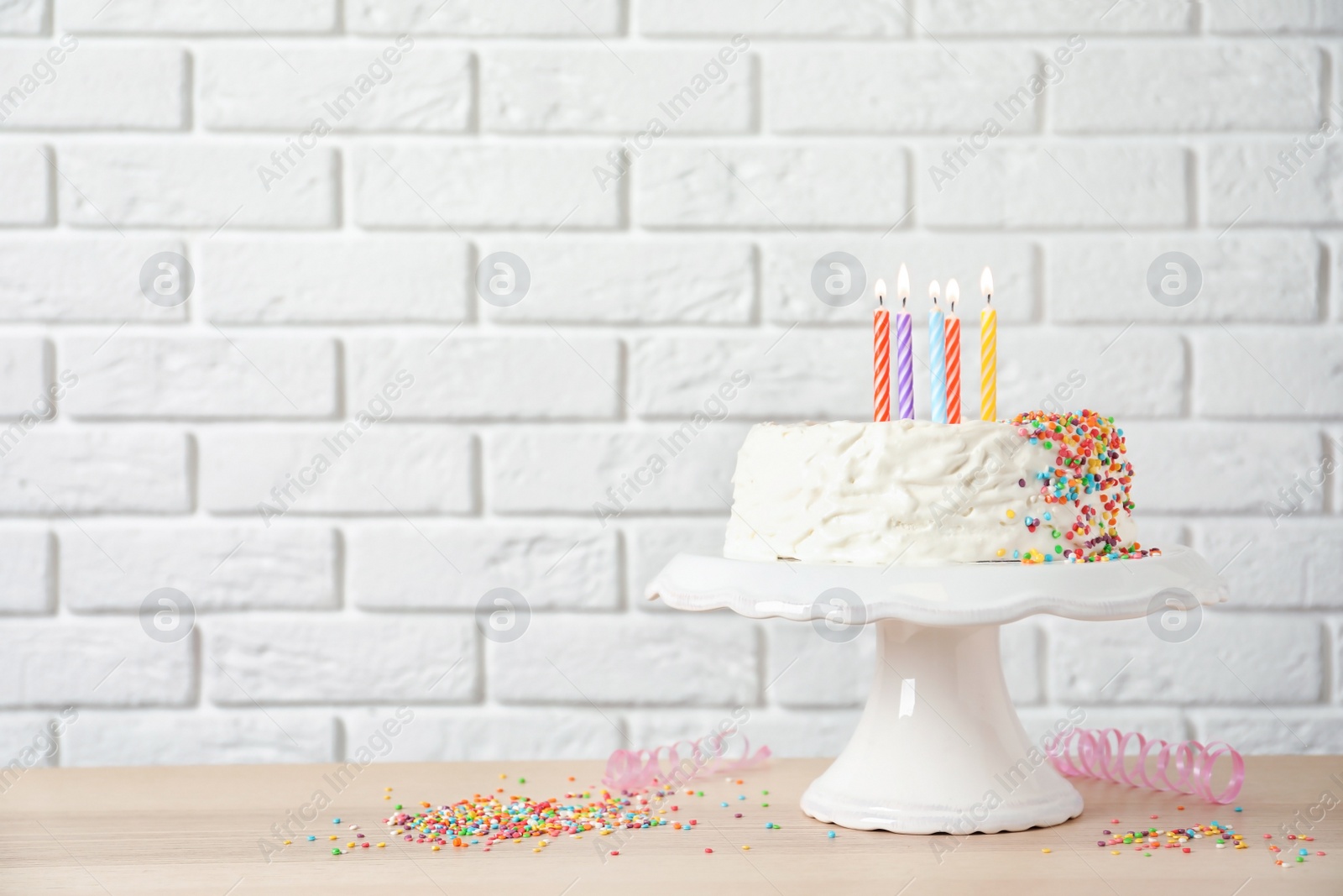 Photo of Birthday cake with candles on table against brick wall