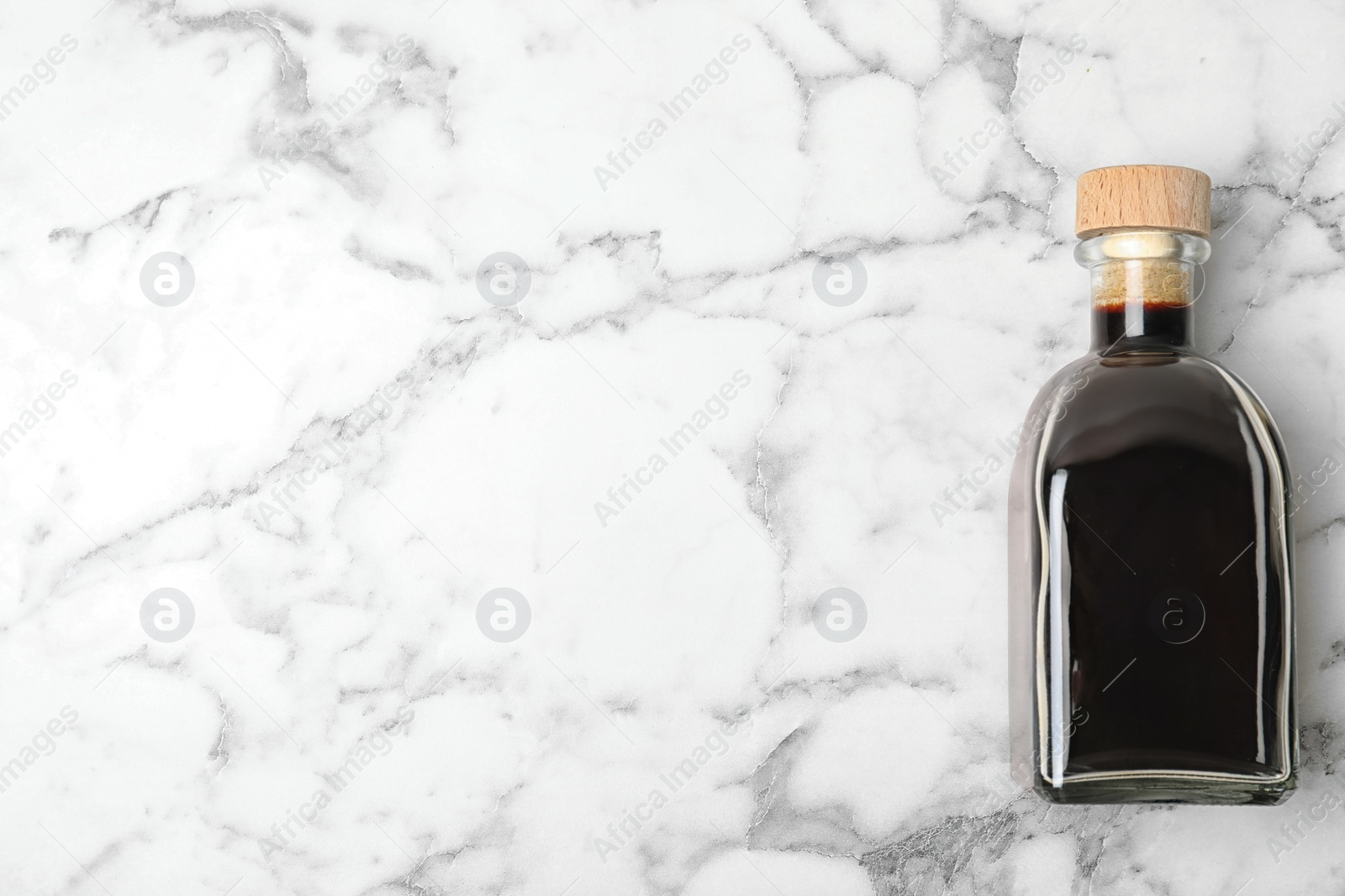 Photo of Balsamic vinegar in glass bottle on marble background, top view. Space for text