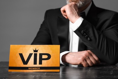 Man sitting at table with VIP sign on grey background, closeup