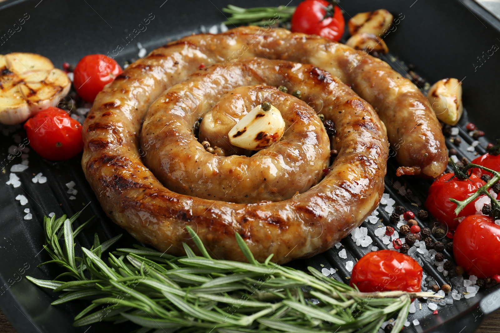 Photo of Delicious homemade sausage with garlic, tomatoes, rosemary and spices in grill pan, closeup