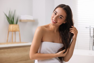 Photo of Young woman applying cosmetic hair mask in bathroom