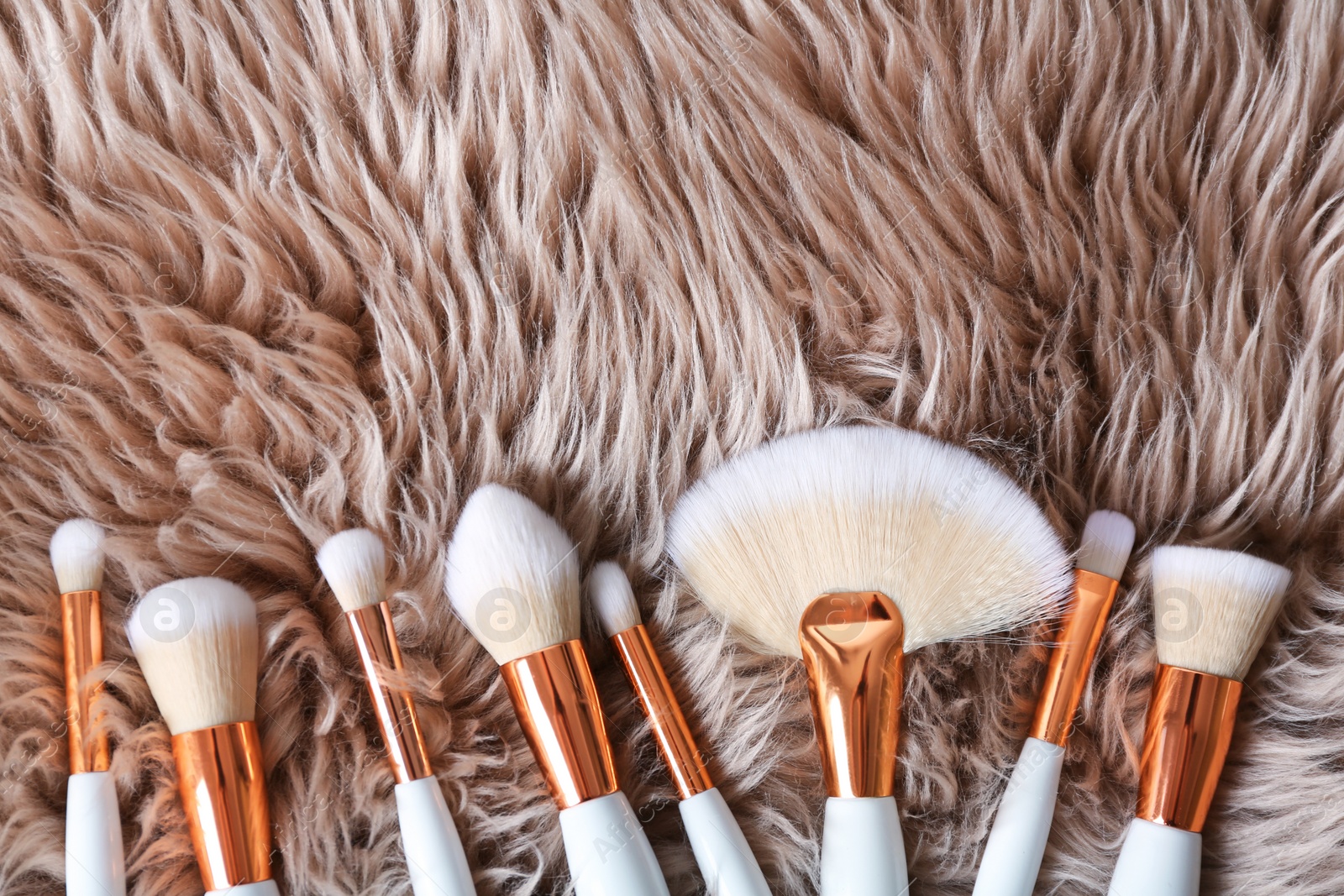 Photo of Flat lay composition of professional makeup brushes on furry fabric. Space for text