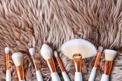 Photo of Flat lay composition of professional makeup brushes on furry fabric. Space for text