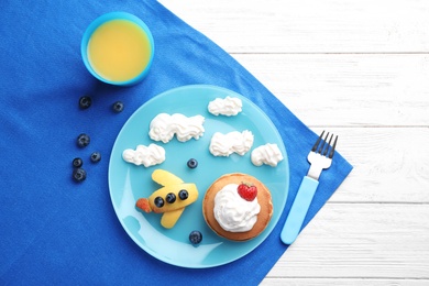 Photo of Tasty pancakes served with berries, whipped cream and juice on white wooden table, flat lay. Creative idea for kids breakfast