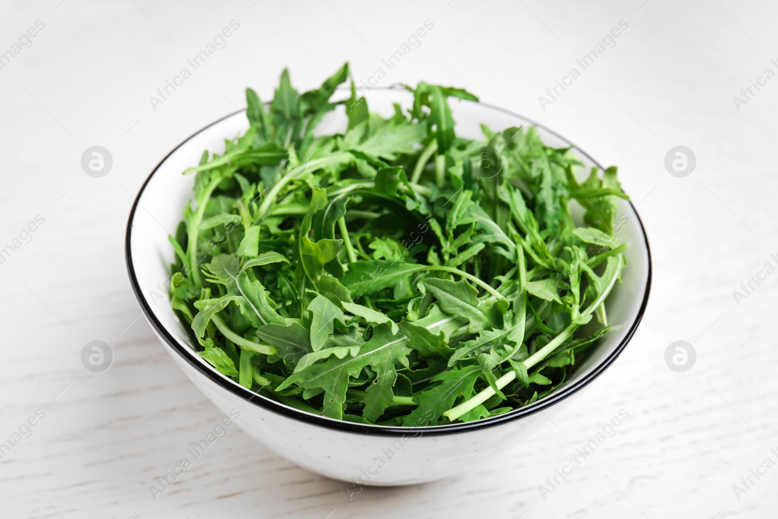 Photo of Fresh arugula in bowl on white wooden table