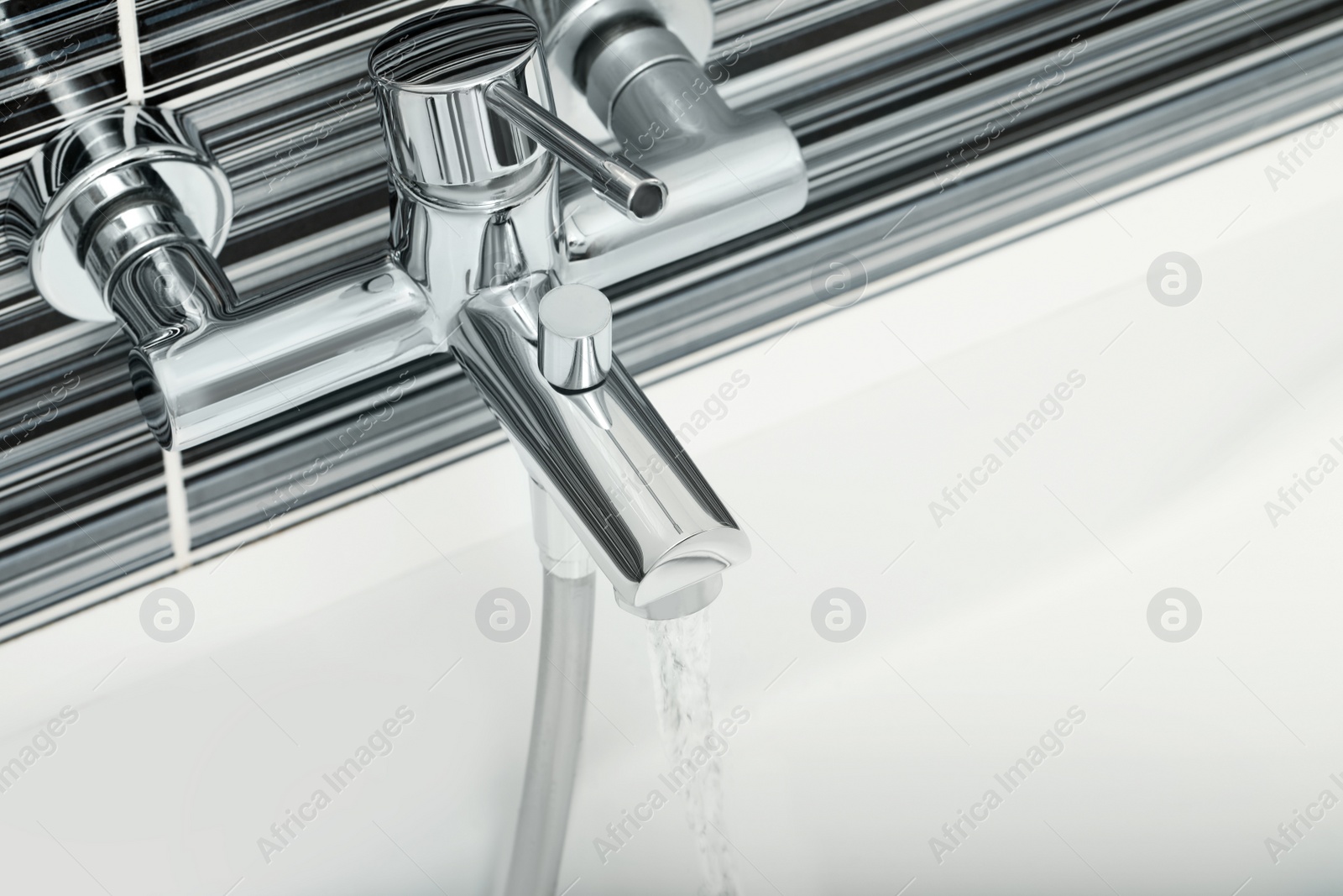 Photo of Water flowing from bath tap installed on black and white wall