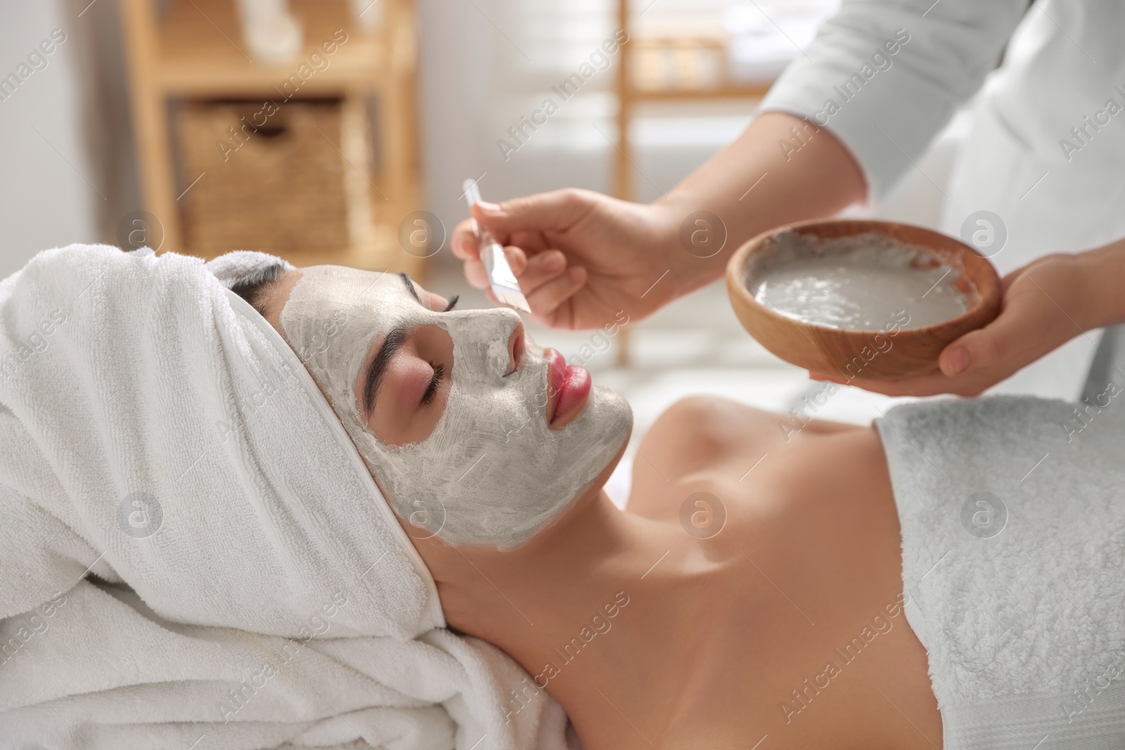 Photo of Cosmetologist applying mask on woman's face in spa salon, closeup