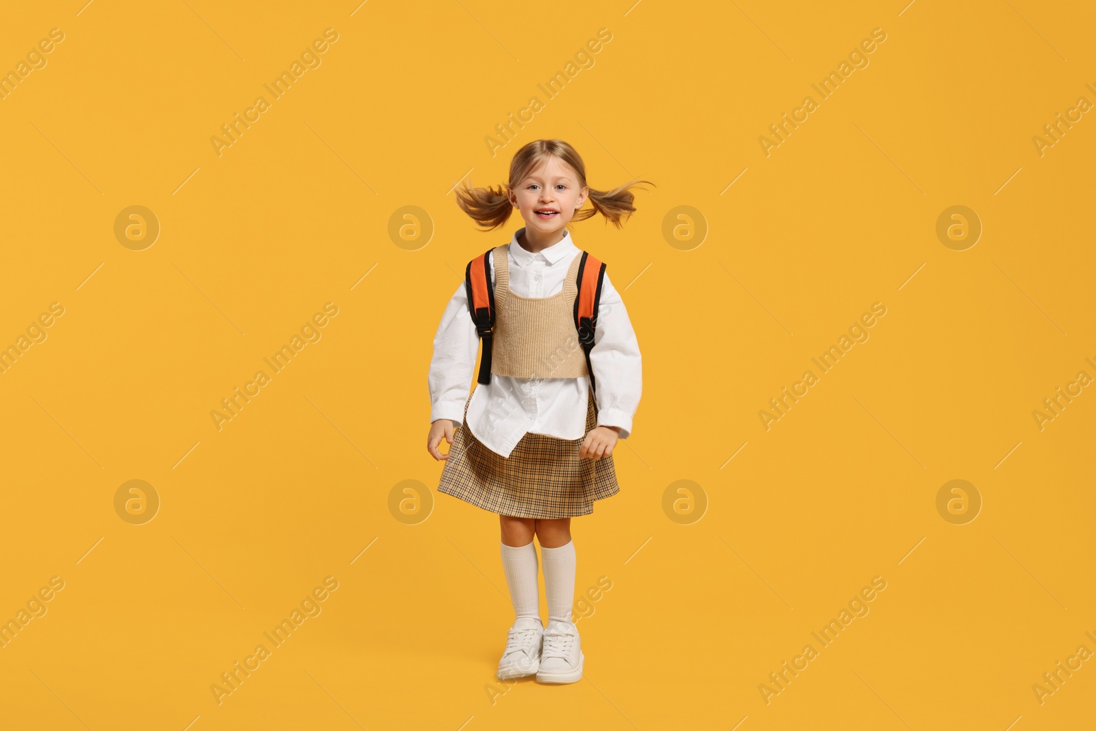 Photo of Happy schoolgirl with backpack on orange background