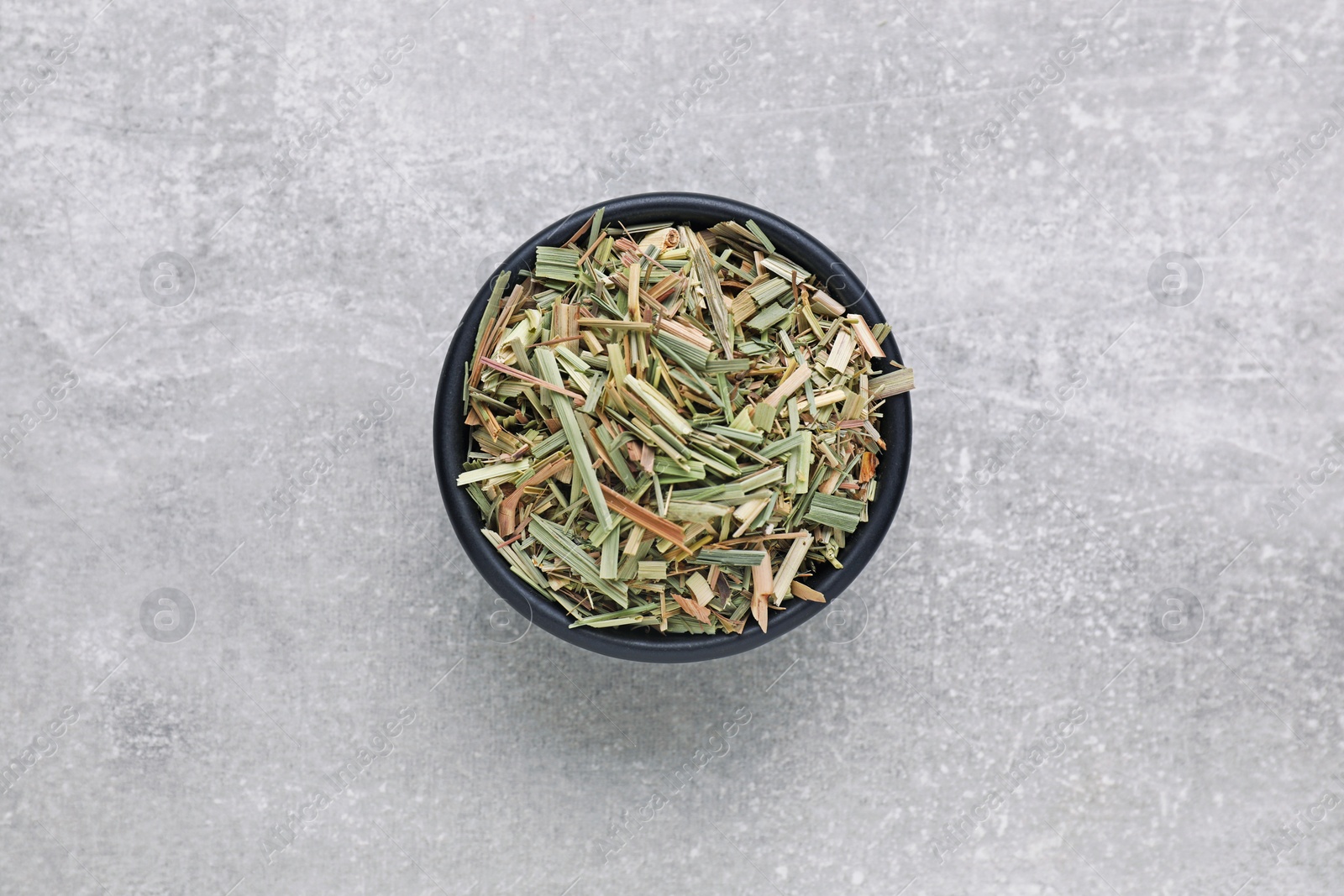 Photo of Bowl with aromatic dried lemongrass on light grey table, top view