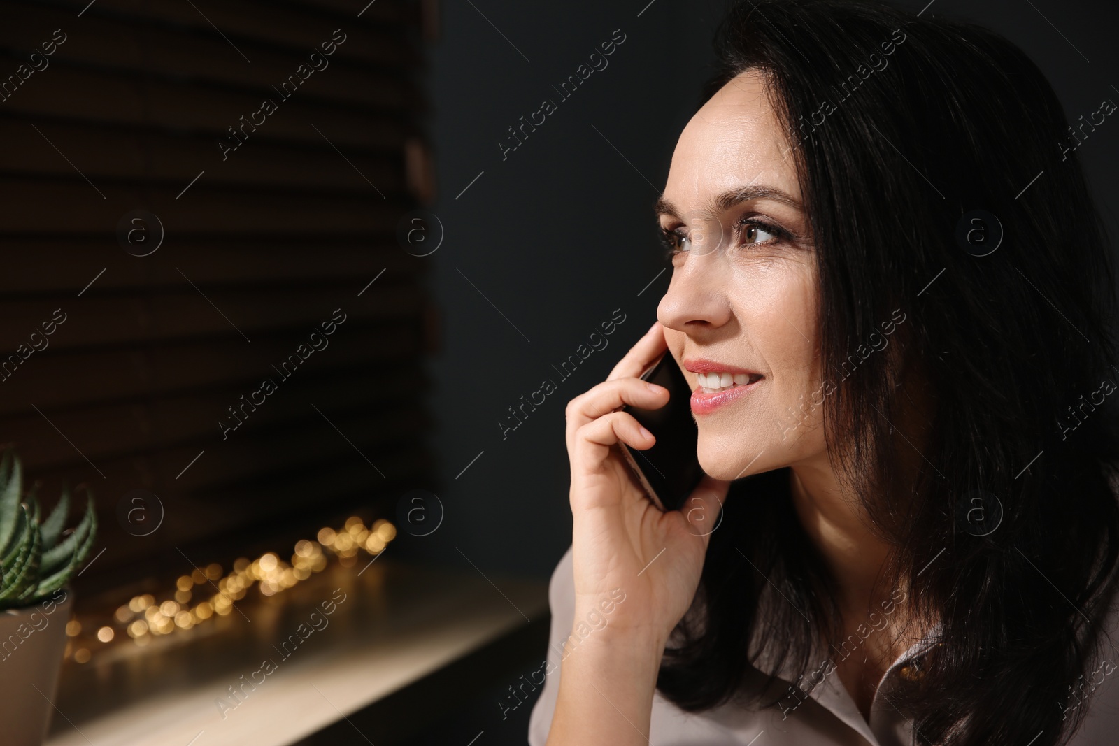 Photo of Beautiful mature woman talking on smartphone at home. Space for text