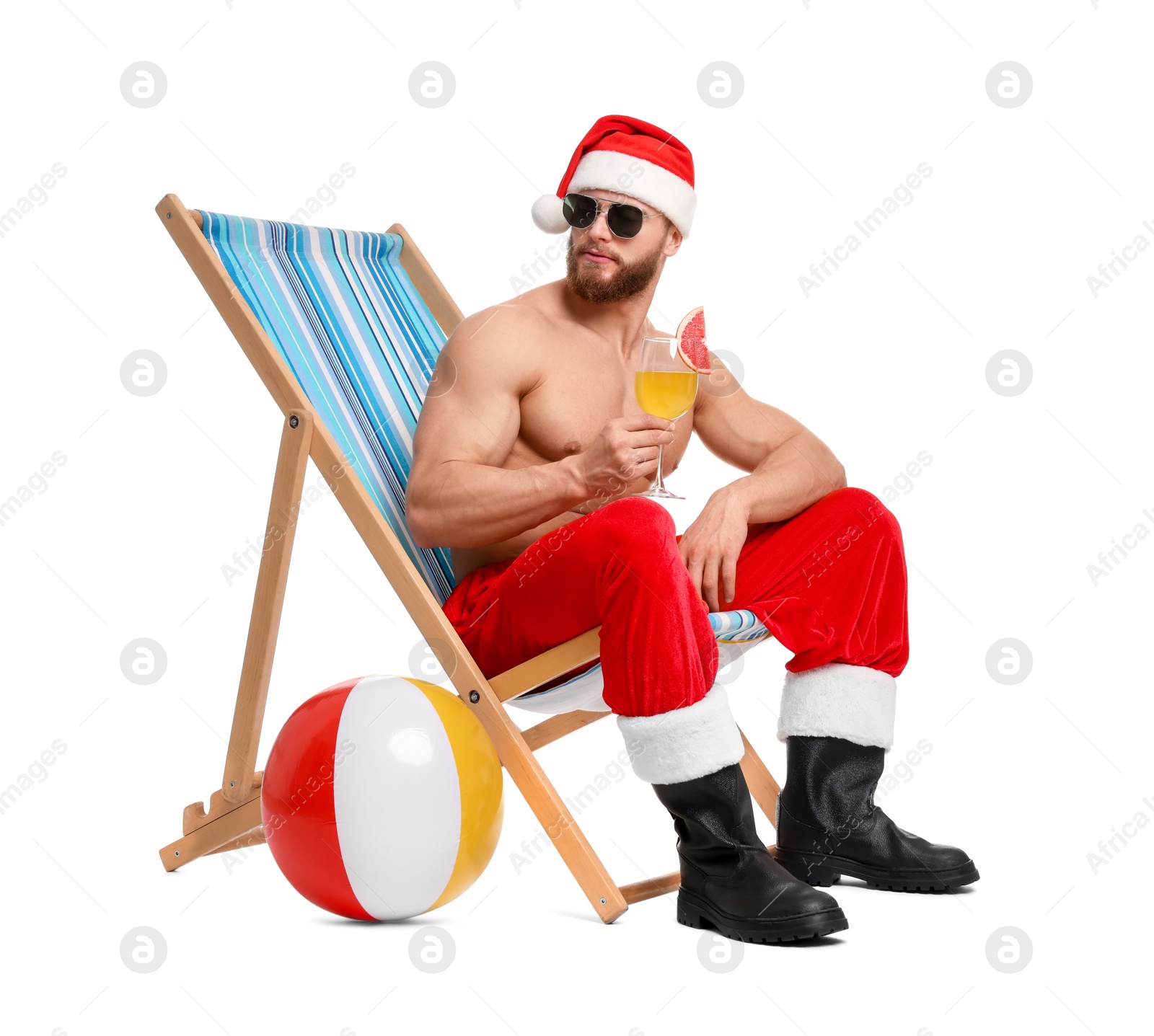 Photo of Muscular young man in Santa hat with deck chair, ball, sunglasses and cocktail on white background