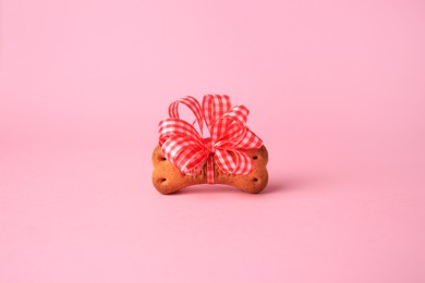 Photo of Bone shaped dog cookie with bright bow on pink background