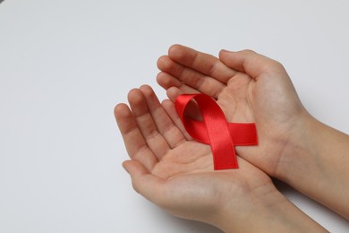 Photo of Little girl holding red ribbon on white background, closeup. AIDS disease awareness