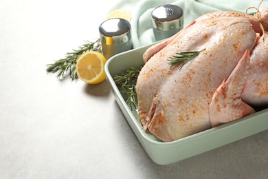 Baking dish with raw spiced turkey and rosemary on table. Space for text