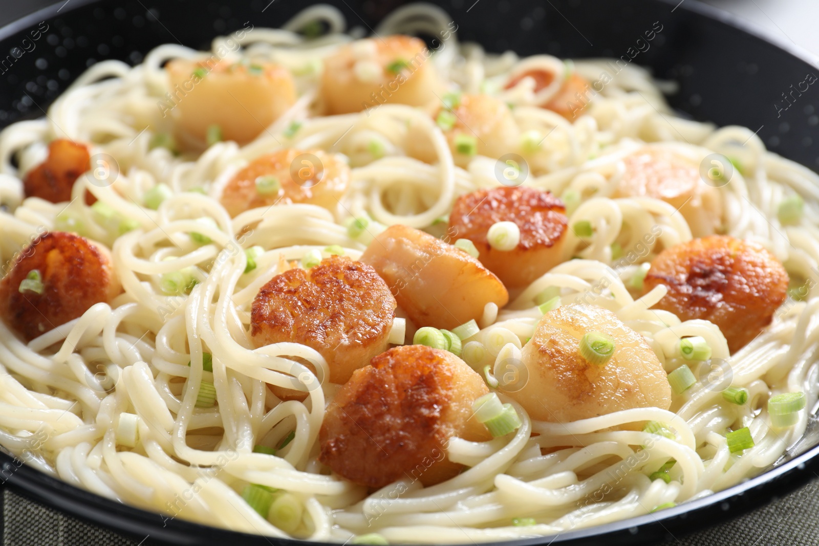 Photo of Delicious scallop pasta with green onion on table, closeup