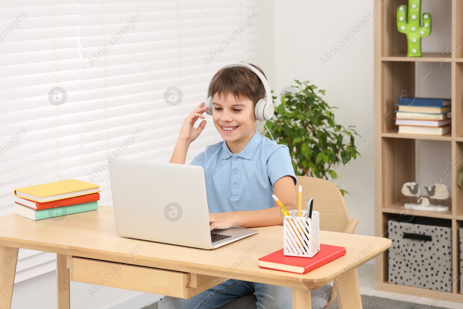 Photo of Boy using laptop and headphones at desk in room. Home workplace