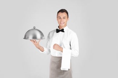 Photo of Waiter holding metal tray with lid on grey background