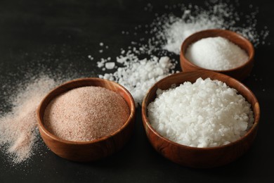 Photo of Different types of organic salt in bowls on black table, closeup