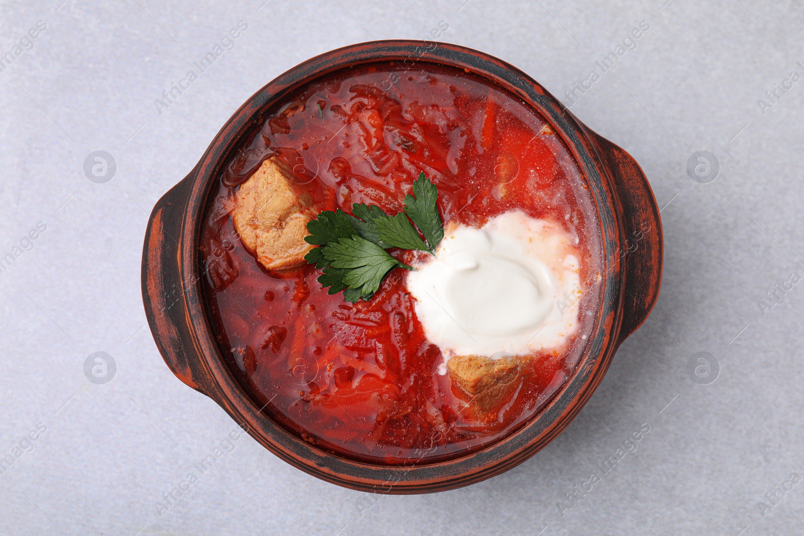 Photo of Tasty borscht with sour cream in bowl on light grey table, top view