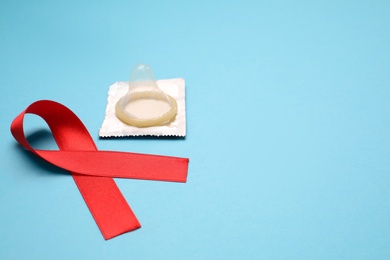 Photo of Red ribbon and condom on light blue background, space for text. AIDS disease awareness